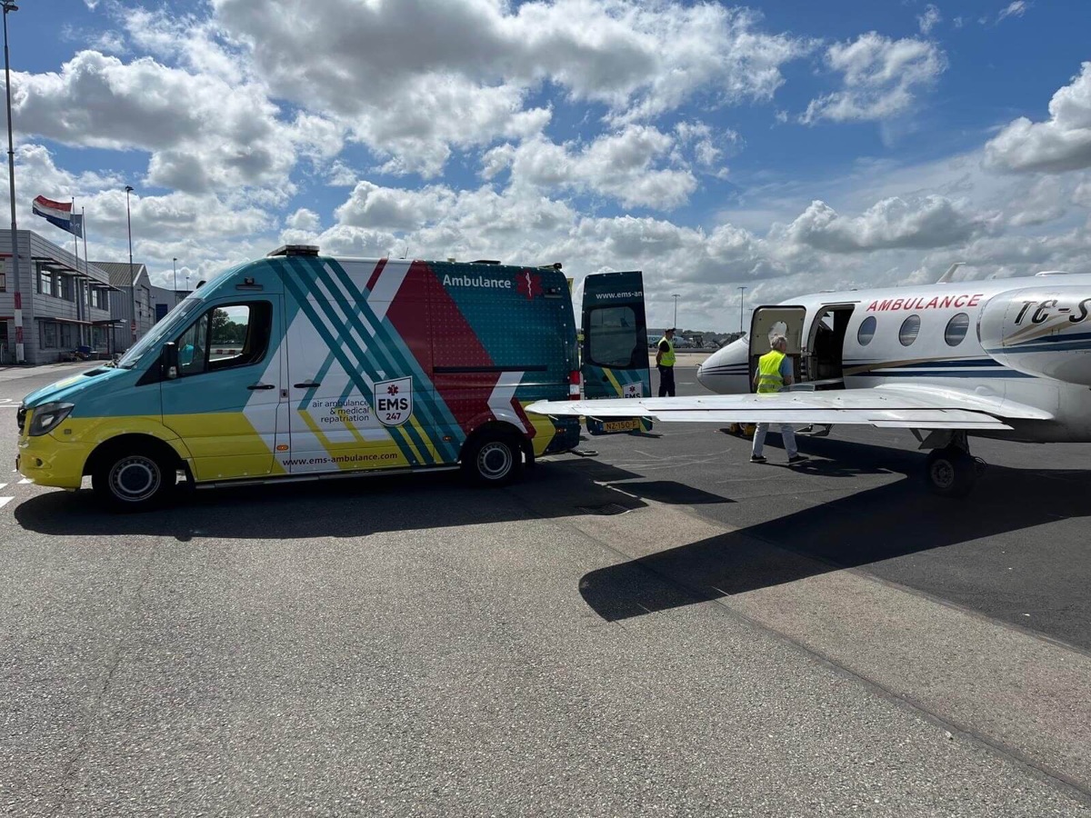 Two EMS ambulances and crew in high-visibility vests beside a jet marked Ambulance, preparing a transfer